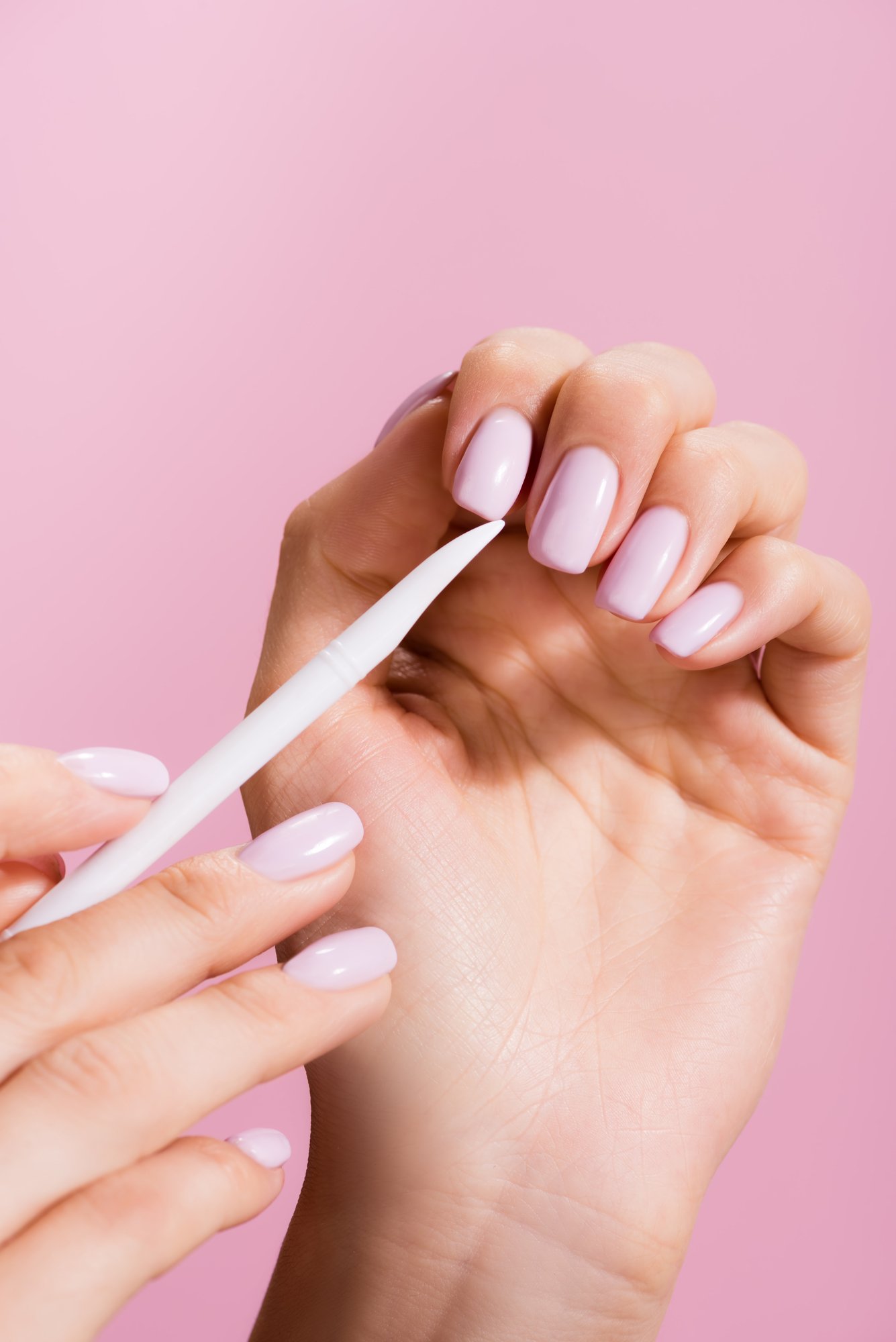 Woman manicuring her long pink nails with a cuticle stick