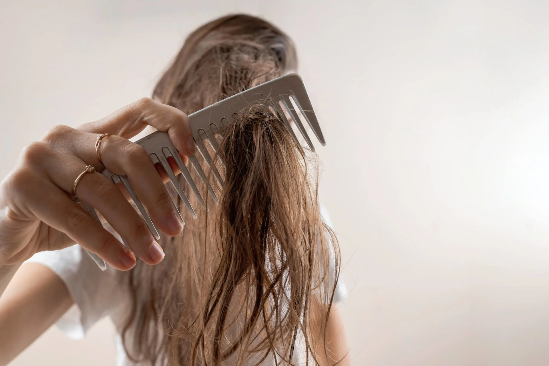 Woman combing her wet brunette hair with a wide-tooth comb pulling out clumps of hair