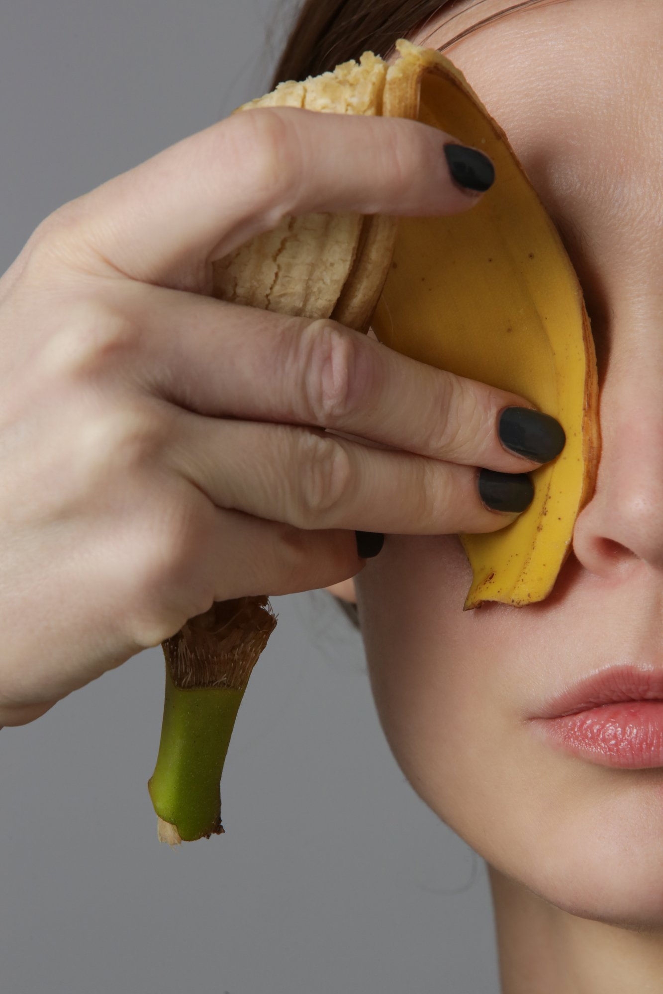 Woman holding a banana peel on her eye area to treat eye wrinkles