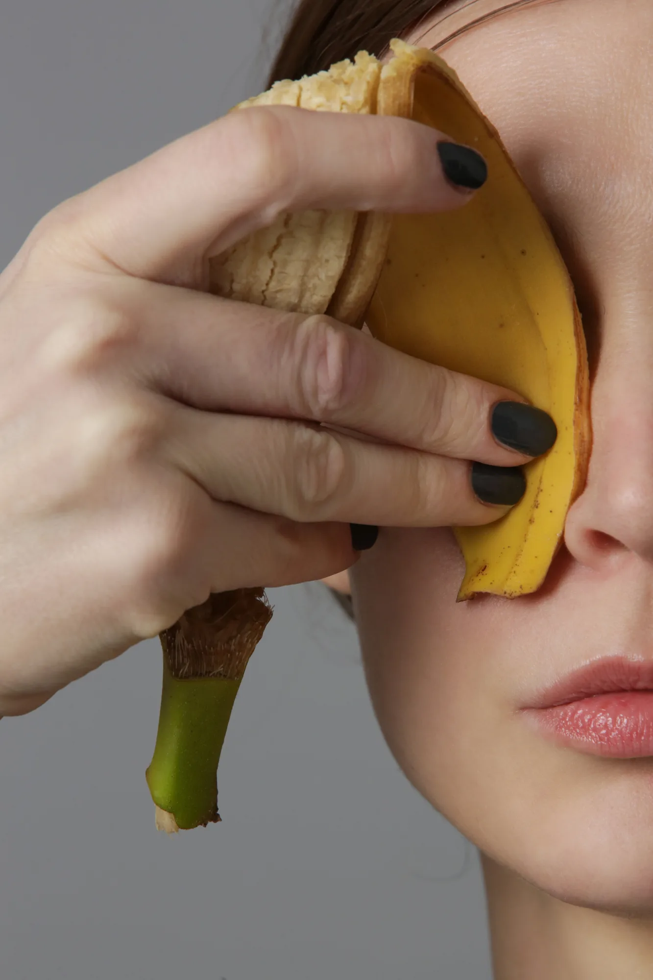 Woman holding a banana peel on her eye area to treat eye wrinkles