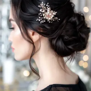 A stunning updo with deep, raven-colored hair styled into a voluminous, twisted chignon. The addition of a delicate floral hairpiece enhances the elegance of the look, perfect for formal occasions. Loose strands frame the face, adding a touch of softness and romance.