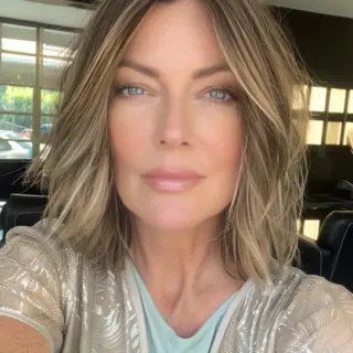 Blonde-highlighted medium shag features stunning dimensional color with darker roots transitioning to brighter face-framing pieces. Natural-looking waves add body and movement to the cut. Longer layers in front gradually become shorter toward the back, creating a subtle A-line effect without being too dramatic. Root shadowing adds depth while bright blonde highlights emphasize the waves.